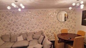 A room with a sectional sofa, a round wooden table, wicker chairs, floral wallpaper, and a ceiling light fixture. - 3 Bed House - Sleeps 6 - Parking - Wifi (Maidstone)