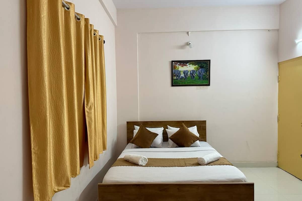 A single bed with a wooden headboard, white bedding, and two brown pillows. A painting of elephants is on the wall above the bed.