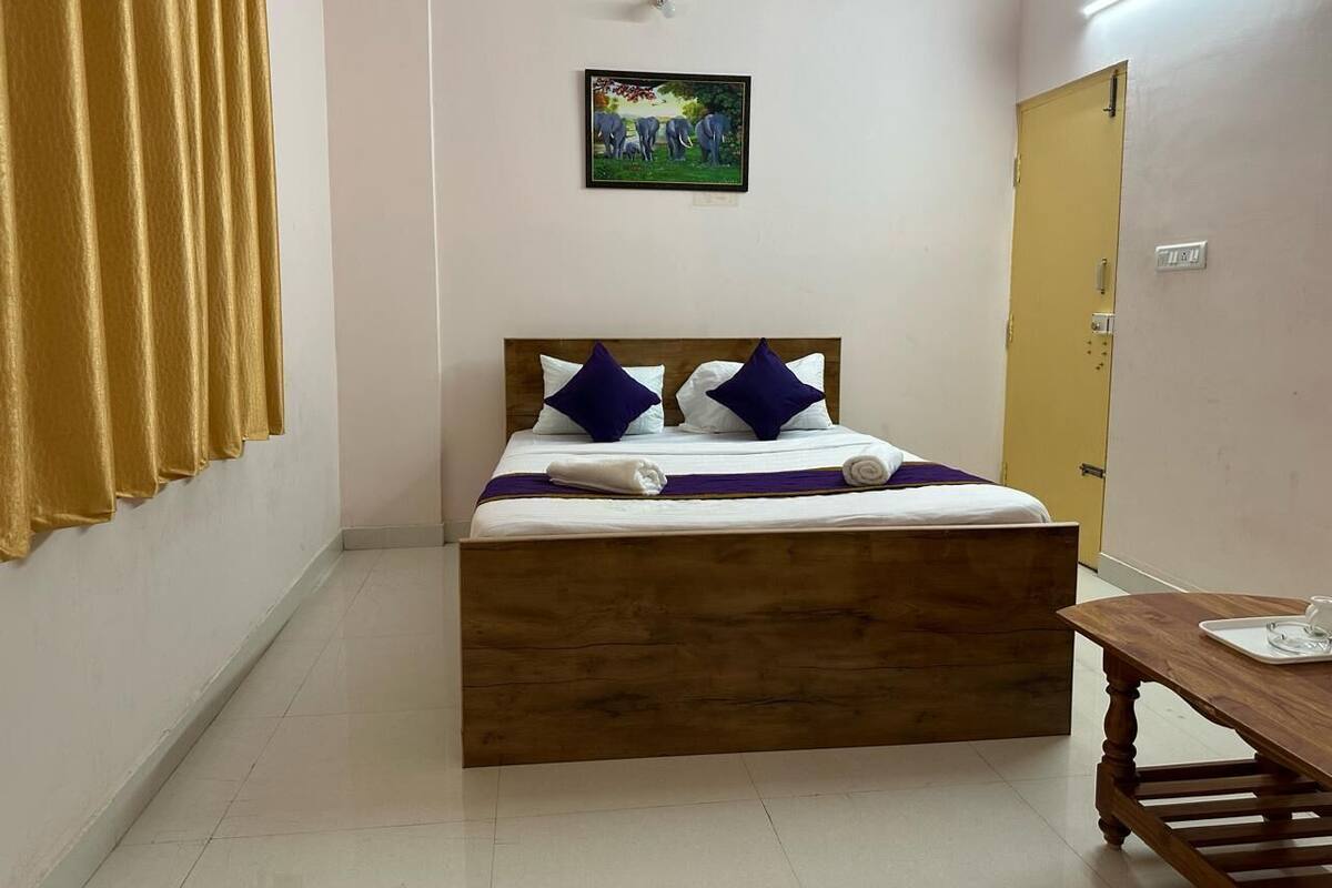 A bedroom with a wooden bed, a small table, a painting on the wall, and a door.