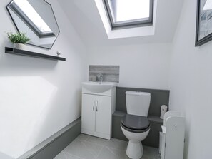 A modern bathroom with a skylight, white fixtures, and a grey tiled floor. - The Coach House (Dolgellau)