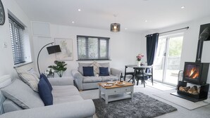 A modern living room with a grey sofa, a coffee table, a fireplace, and a dining area with a table and chairs.
