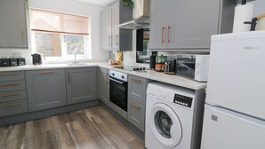 A modern kitchen with grey cabinets, a built-in oven, a washing machine, and a microwave.