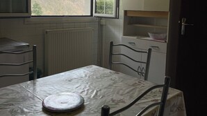 Eine Küche mit Tisch, Stühlen, Schränken und einem Fenster mit Blick auf einen Wald.