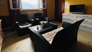 Ein Hotelzimmer mit Sofa, einem kleinen Tisch, einem Fernseher und einem Fenster mit Vorhängen.