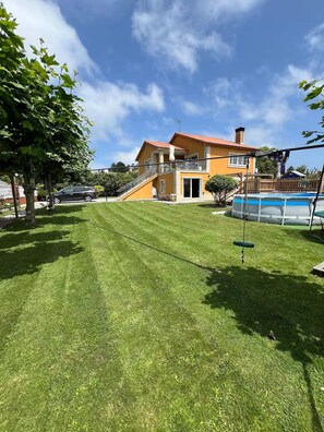 A house with a swimming pool, a well-maintained lawn, and a staircase leading to the balcony.