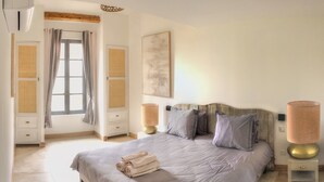Ein Schlafzimmer mit einem großen Bett, zwei Nachttischen mit Lampen, einem Fenster mit Vorhängen und einem Wandbild.