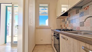 A narrow kitchen with a tiled backsplash, a window with a view, and a door leading outside.