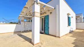 A residential building with a covered patio, a door with blue shutters, and a clear sky.