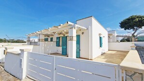 A small white building with a pergola, blue shutters, and a gated entrance.