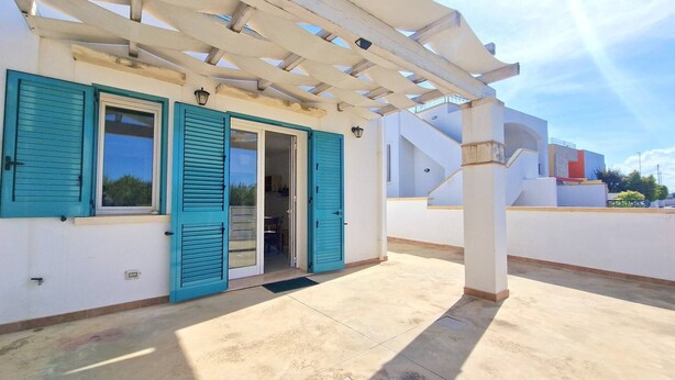 A covered outdoor area with a white pergola, a door with teal shutters, and a view of the surrounding buildings.