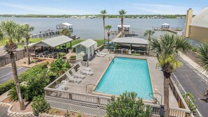 A pool area with a view of the water, deck chairs, and palm trees.