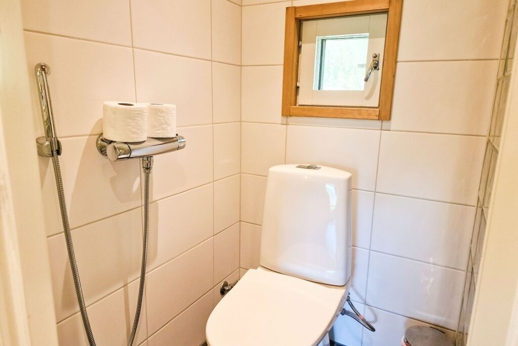 Een kleine betegelde badkamer met toilet, douche en raam.