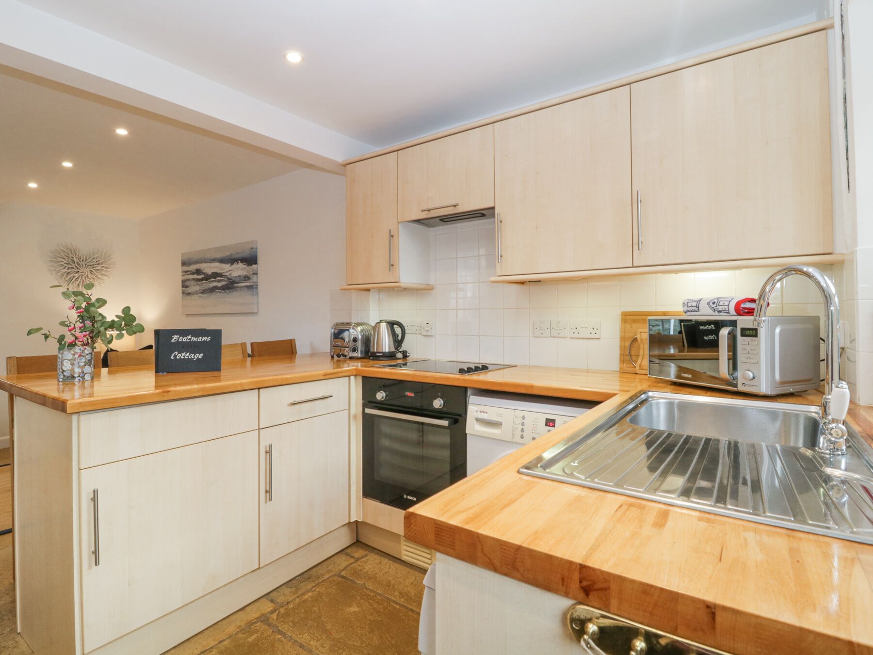 A modern kitchen with wooden cabinets, a Bosch dishwasher, a microwave, and a sink.