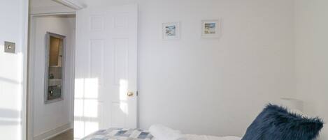 A bedroom with a bed, a window, a door, and a small wall-mounted shelf.