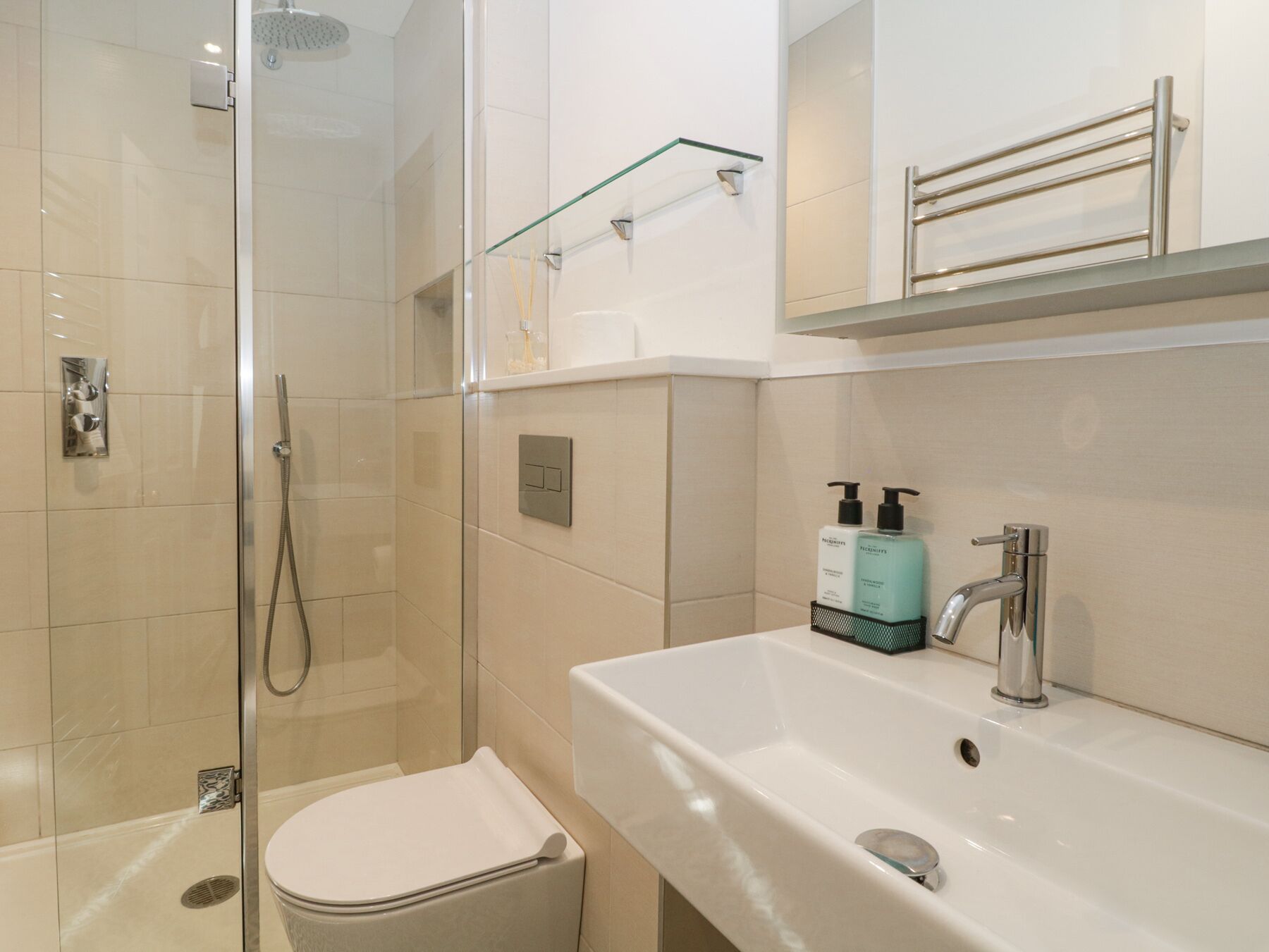 A modern bathroom with a glass-enclosed shower, a white sink with a silver faucet, and a toilet.