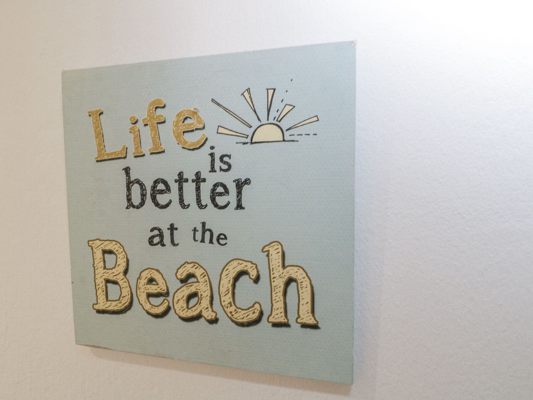 Uma parede com uma placa que diz 'Life is better at the Beach'.