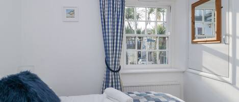 Ein Schlafzimmer mit einem Bett, einem Fenster mit Blick auf Palmen und einem karierten Vorhang.