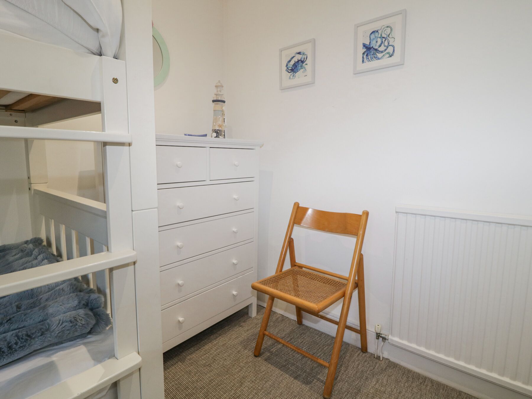 A room with a bunk bed, a dresser, a chair, and two framed artworks on the wall.