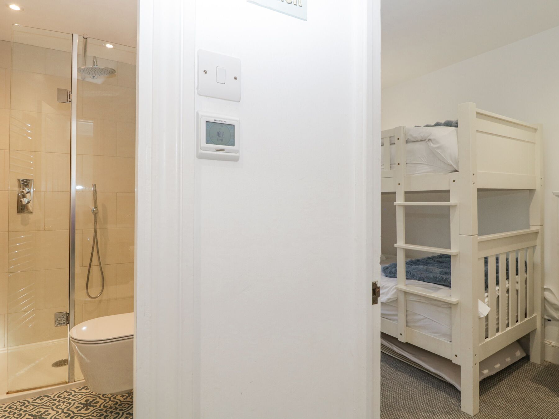 Une salle de bain avec une douche à parois de verre, des toilettes et un lit superposé.