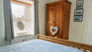 A bedroom with a bed, a wooden wardrobe, a window with curtains, and framed pictures on the wall. - 63 Kingsland Road (Holyhead)