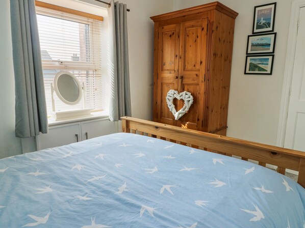 A bedroom with a bed, a wooden wardrobe, a window with curtains, and framed pictures on the wall. - 63 Kingsland Road (Holyhead)