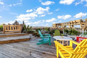 Una terraza de madera con sillas y una mesa, rodeada por una valla y plantas.