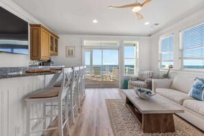 Una cocina con muebles blancos, una zona de comedor con sillas blancas, una mesa de centro de madera y vistas al exterior.