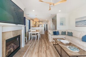 A spacious living room with a fireplace, a dining area, a kitchen, and a staircase leading to another level.