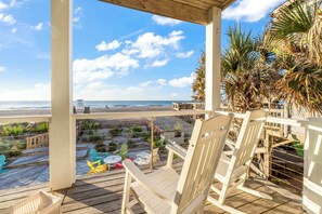 Terraza de madera con sillas y mesas con vista a la playa.