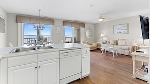 A spacious living area with a large window overlooking a balcony, a kitchen with white cabinetry, and a cozy seating area with a sofa and coffee table.