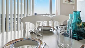 A dining table with plates, glasses, and a vase, set against a window with blinds.