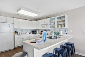 Una cocina moderna con armarios blancos, una isla central con taburetes, un microondas y una cafetera.