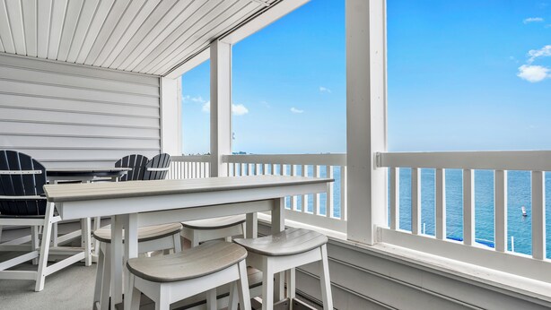 A balcony with a view of the sea, a white table, and matching chairs.
