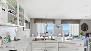 A modern kitchen with a central island, a dining area with a view, and a living space with a sofa and a clock.
