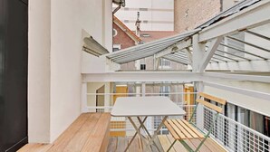Un petit balcon extérieur avec un plancher en bois, une table blanche et un banc.