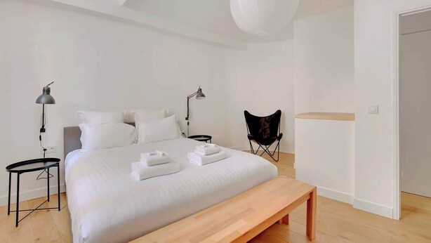 Une chambre moderne avec un grand lit, deux tables de chevet, une chaise et un luminaire suspendu.