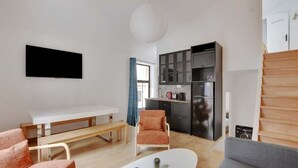 Un salon moderne avec un canapé blanc, un banc et une table à manger. Il y a également un coin cuisine avec des placards et des appareils électroménagers.