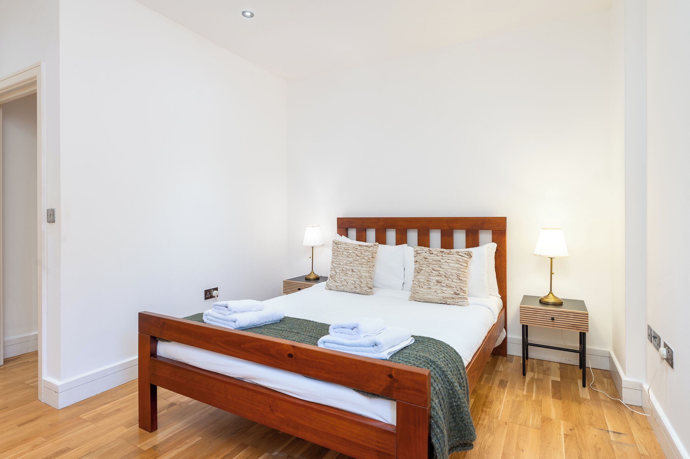 A neatly made bed with a wooden headboard, two bedside tables with lamps, and a wooden floor.