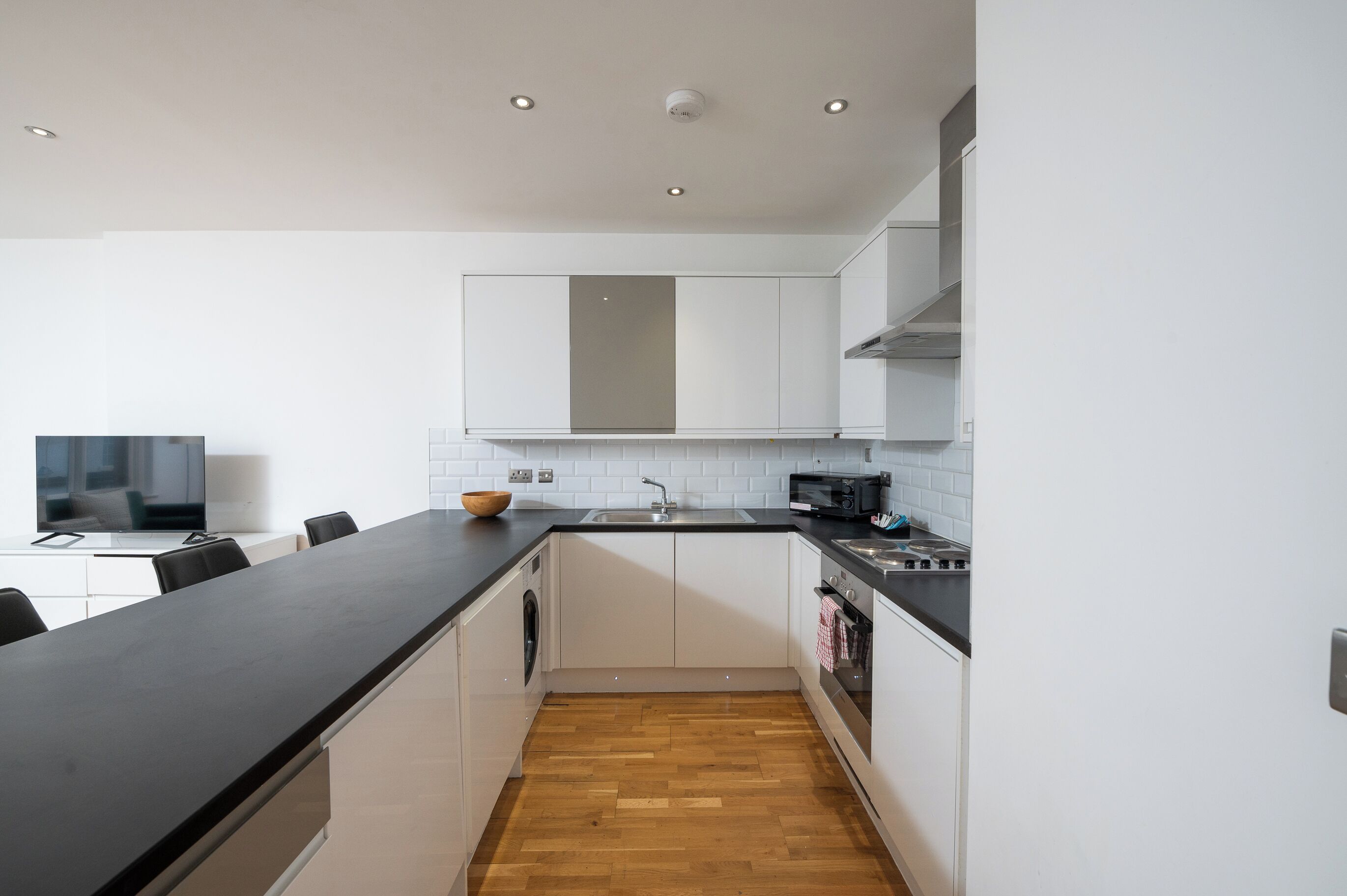 A modern kitchen with white cabinets, a black countertop, and a wooden floor.
