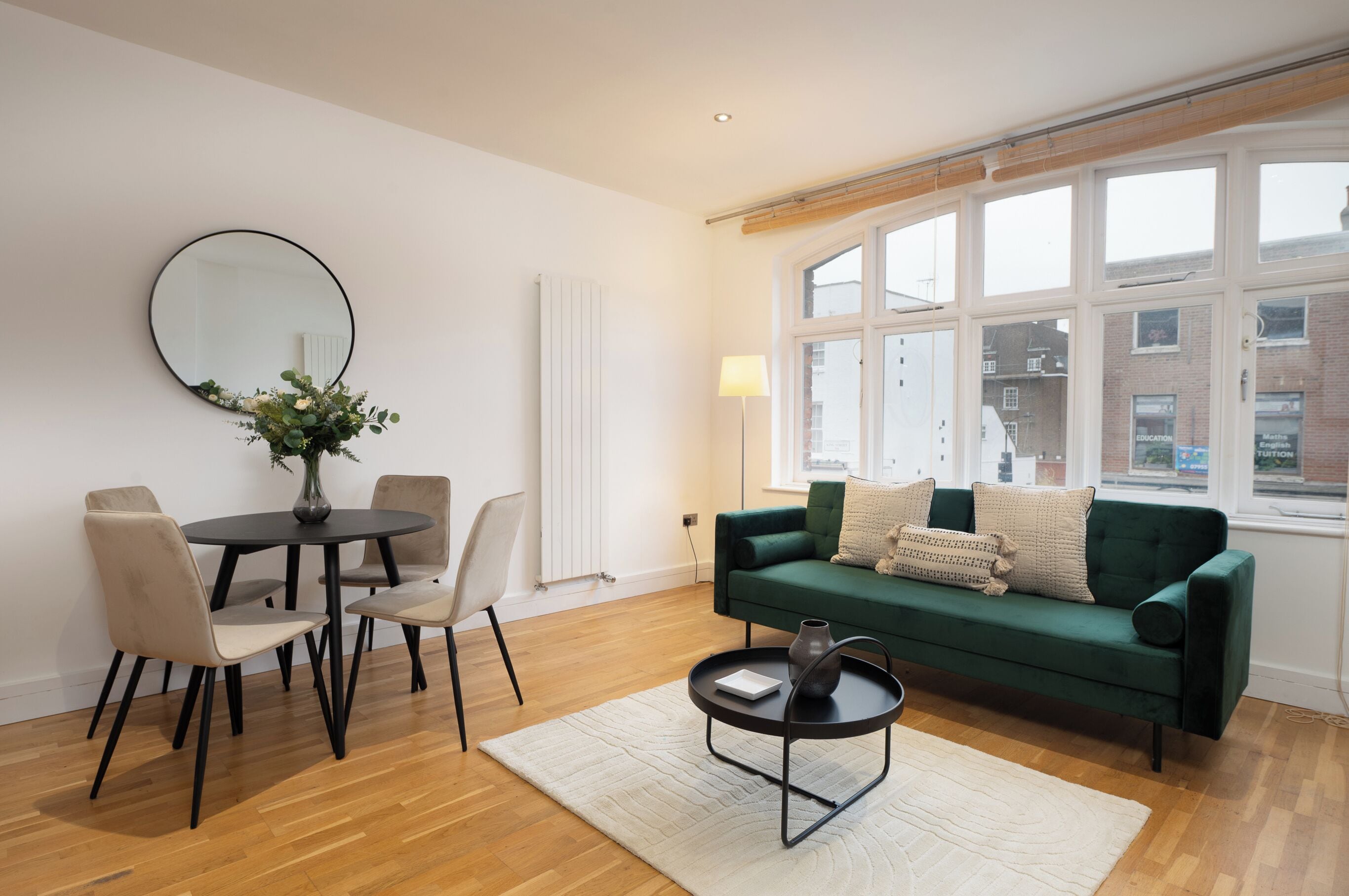 A modern living room with a round dining table, chairs, a green sofa, and a large window.