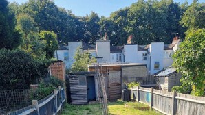 Un jardin avec une clôture en bois, un portail en métal et un petit abri de jardin.
