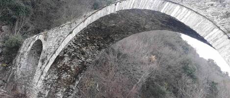 A stone bridge with multiple arches over a river, surrounded by trees and hills.