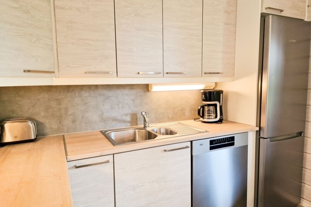Una cocina moderna con alacenas de madera clara, un lavamanos de acero inoxidable, una cafetera y un lavavajillas.