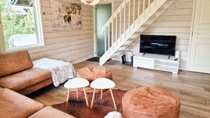 A modern living room with a wooden floor, a brown sofa, two white round tables, and a television on a white stand. - Villa Rantatuuli, Himosranta (Keski-Suomi)