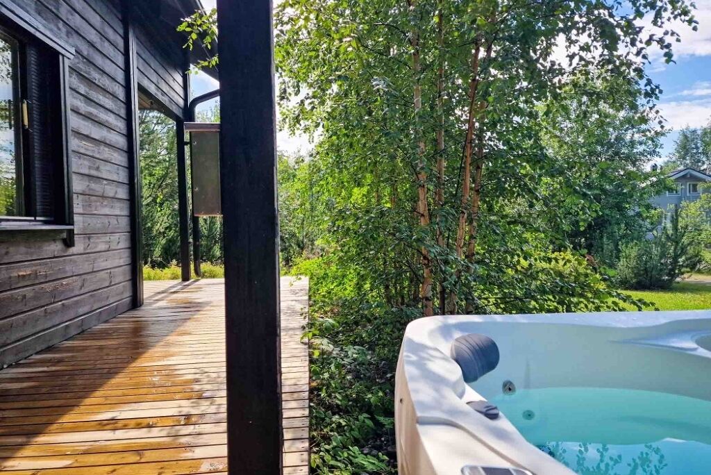 A wooden deck leading to a hot tub in a lush garden setting.
