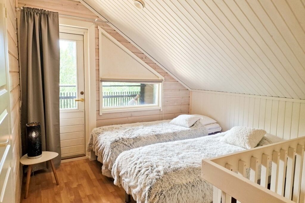 A cozy attic bedroom with two beds, a window with a view of a wooden deck, and a door with a curtain.