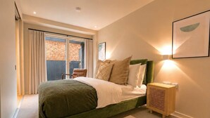 A bedroom with a bed, a chair, a bedside table, and a window with curtains.
