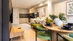 A modern kitchen with a dining area, a TV mounted on the wall, and a large vase with plants.