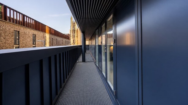 A corridor with a metal railing, a tiled floor, and large windows.