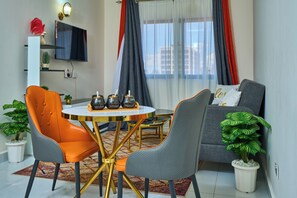 A modern living room with a round table, two chairs, a sofa, and a television. - Luxore Apartments (Syokimau)